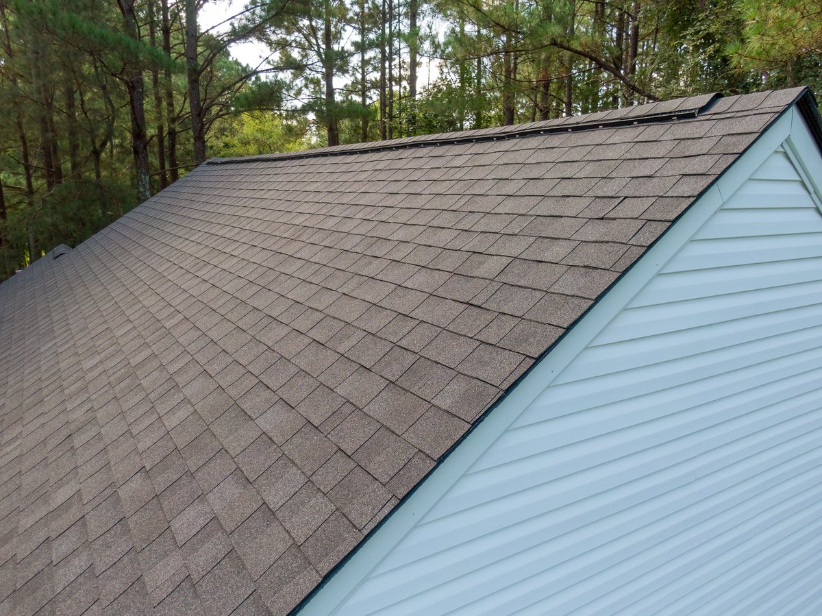 Aerial view of newly installed architectural asphalt shingle roof with driftwood color palette, showing clean edge cuts and uniform courses on a residential home
